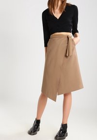 Tan wrapkjol med knytning vid waist, midilängd, i kombination med en svart åtsittande topp och glänsande svarta ankelstövlar. Slät tygstruktur.