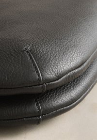 Gros plan sur un cuir noir texturé avec une couture détaillée, montrant deux surfaces rembourrées empilées, probablement des parties de sacs ou de meubles.