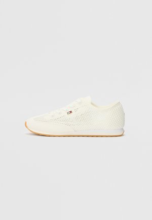 Hvit mesh-sneaker med et teksturert design, har rund tå, snøring og en kontrasterende gummisåle. Merkverdig logo-detallering på siden.