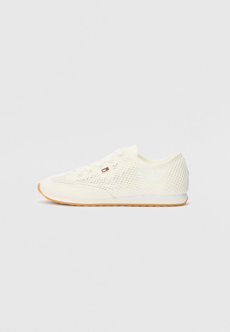 White mesh sneaker with a textured design, featuring a rounded toe, laces, and a contrasting rubber sole. Notable logo accent on side.