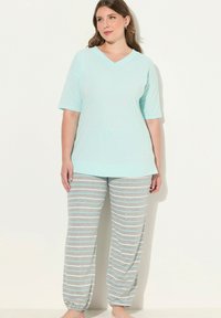 Světle modré tričko s výstřihem do V v kombinaci se šedými pruhovanými kalhotami, které mají světle modré pruhy, volný střih, měkkou látku a elastické manžety u kotníků.