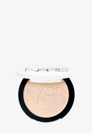 NARS highlighter i en rund kompakt med hvit lokk og svart bunn, som har en glitrende gullchampagnefarge med preget logo detaljer.