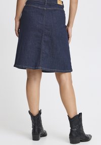 Mörk denimkjol med en utställd design och synlig sömnad. Kombinerad med svarta cowboyboots med dekorativ sömnad och en kraftig klack.