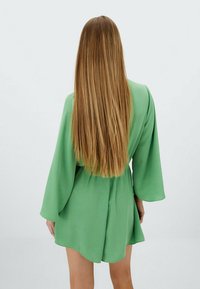 Vestido verde con cinturón, de mangas largas y fluidas, con un dobladillo corto, hecho de una tela ligera y de textura suave.