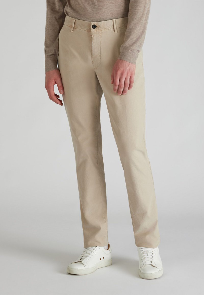 Chinos beiges de algodón con corte recto, que presentan un cierre frontal con botón, bolsillos laterales y se combinan con zapatillas blancas.