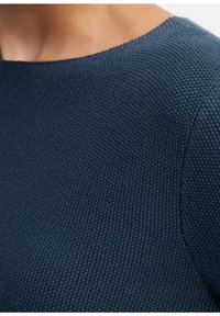 Dunkelblauer Strickpullover mit strukturiertem Muster, rundem Ausschnitt und glatter Oberfläche. Nahaufnahme des Stoffes und der Nähdetails.