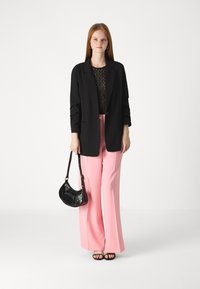 Črn blazer preko čipkaste bluze, v kombinaciji z roza hlačami z visokim pasom. Dodatki vključujejo črno torbico čez ramo in črne sandale.