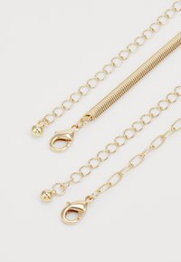 Gold chain accessory featuring a mix of interlocking links, a textured coil segment, and two clasp closures for secure attachment.