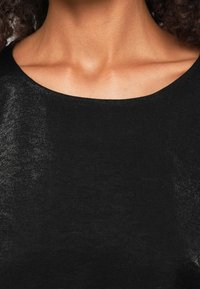 Gros plan sur le cou et la partie supérieure de la poitrine d'une personne portant un t-shirt noir à col rond, avec des cheveux bouclés foncés partiellement visibles.