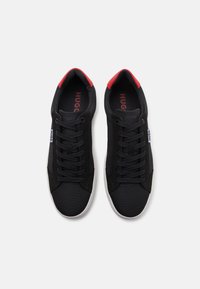 Svarta sneakers med röda detaljer, övre del i tyg, rund tå och platt gummisula. Utrustad med svarta snören och "HUGO"-logotyp på inläggen.