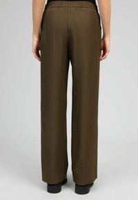 Pantalons larges marron en tissu fluide, avec une taille haute et une finition soignée à l'ourlet, associés à des chaussures noires.