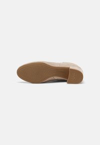 Semelle de chaussure en daim beige montrant une bande de roulement en caoutchouc antidérapante texturée et un talon bloc avec l'inscription "ANTI SLIDE" en relief sur le talon.