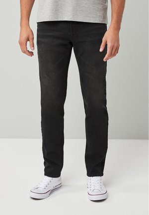Jeans de mezclilla negros con un corte ajustado, que cuentan con una textura suave y un diseño clásico de cinco bolsillos. Combinados con zapatillas blancas.