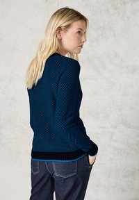Suéter de punto en navy con un patrón texturizado, con acentos azules y un dobladillo negro acanalado. Combinado con pantalones de mezclilla oscuros.