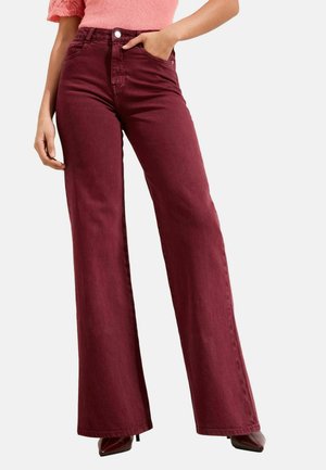 Woman wearing high-waisted, wide-leg burgundy pants paired with burgundy pointed-toe heels and a coral knit top.