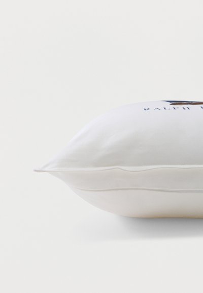 Λευκό ορθογώνιο μαξιλάρι με ορατές ραφές και μερικώς ορατό κεντητό κείμενο και έμβλημα στην επάνω πλευρά.