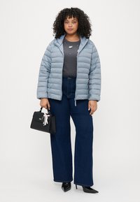 Gaiši zilas pūkainas virsjakas ar kapuci, pelēka T-krekls, kas rotāts ar rotājumiem, tumši zilas platās bikses un maza melna somiņa.