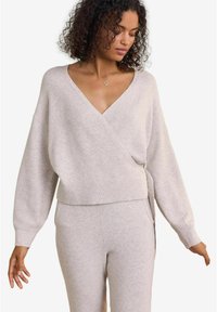 Svetra v svetlo sivi barvi, zavita, iz mehkega pletenega materiala, z V-izrezom, oversized rokavi in ribastimi detajli na robu. Ustvarjeno v kombinaciji z usklajenimi hlačami.