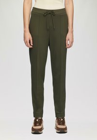 Olijfgroene taps toelopende joggingbroek met een trekkoord in de taille, zijzakken en verticale naden, gecombineerd met bruine en beige sneakers.