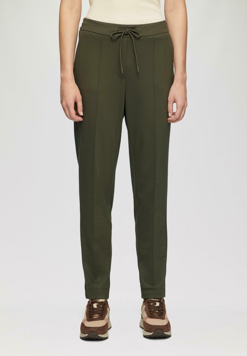 Olijfgroene taps toelopende joggingbroek met een trekkoord in de taille, zijzakken en verticale naden, gecombineerd met bruine en beige sneakers.