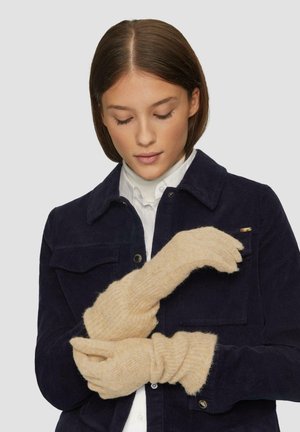 Beige gestrickte Handschuhe mit einem gerippten Muster und einem umgeschlagenen Bündchen. Der Träger hält einen Handschuh und zeigt dabei das weiche Material und das Design.