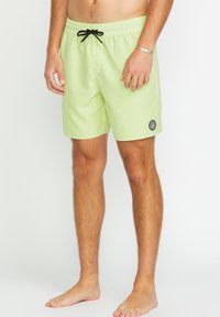 Costumi da bagno verde chiaro con cintura elastica, cordino nero, tasche laterali e un piccolo logo rotondo sulla gamba sinistra in basso.