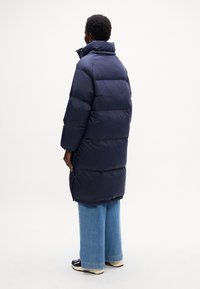 Cappotto puffer blu navy con colletto alto e vestibilità oversize, caratterizzato da cuciture orizzontali, tasche laterali e lunghezza a metà coscia.