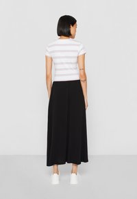 Hvit kortermet topp med rosa og blå striper, parret med et langt svart skjørt, sammen med hvite joggesko; enkel og moderne design.