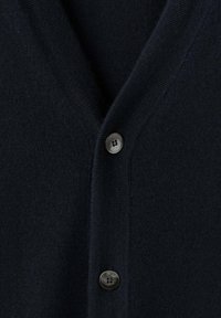 Granatowy kardigan z dekoltem w serek, dzianym wzorem i ciemnymi guzikami. Zbliżenie ukazuje jednolitość tkaniny i przeszycia.