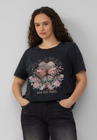 Zwarte katoenen T-shirt met korte mouwen, met een vlinder- en bloemenprint in roze en teal, versleten halslijn, gedragen met donkere jeans.