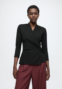 Čierny dlhý rukáv zavinovací top s výstrihom do tvaru V, s nariaseným detailom v páse. Spárovaný s voľnými bordovými nohavicami. Hladká textúra.