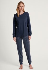 Marineblauwe top met lange mouwen en ronde hals, gecombineerd met marineblauwe pyjamabroek met stippen. De stof lijkt zacht en comfortabel te zijn.