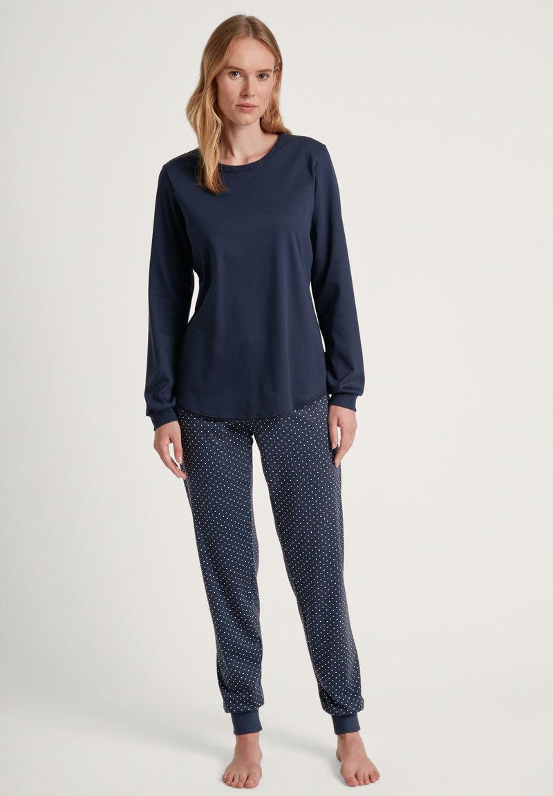 Marineblauwe top met lange mouwen en ronde hals, gecombineerd met marineblauwe pyjamabroek met stippen. De stof lijkt zacht en comfortabel te zijn.
