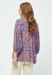 Blusa fluida viola con un motivo floreale in rosa e arancione. Presenta maniche a sbuffo, una vestibilità ampia e un tessuto morbido e leggero.