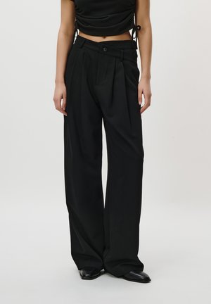 Black high-waisted trousers with pleats, made of smooth fabric. Features a button closure and wide, flowing leg design.
