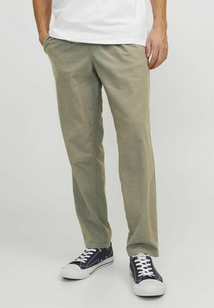 Olivgrüne Chinos aus atmungsaktivem Stoff, mit einem lockeren Schnitt, seitlichen Taschen und kombiniert mit marineblauen Sneakers mit weißen Sohlen.