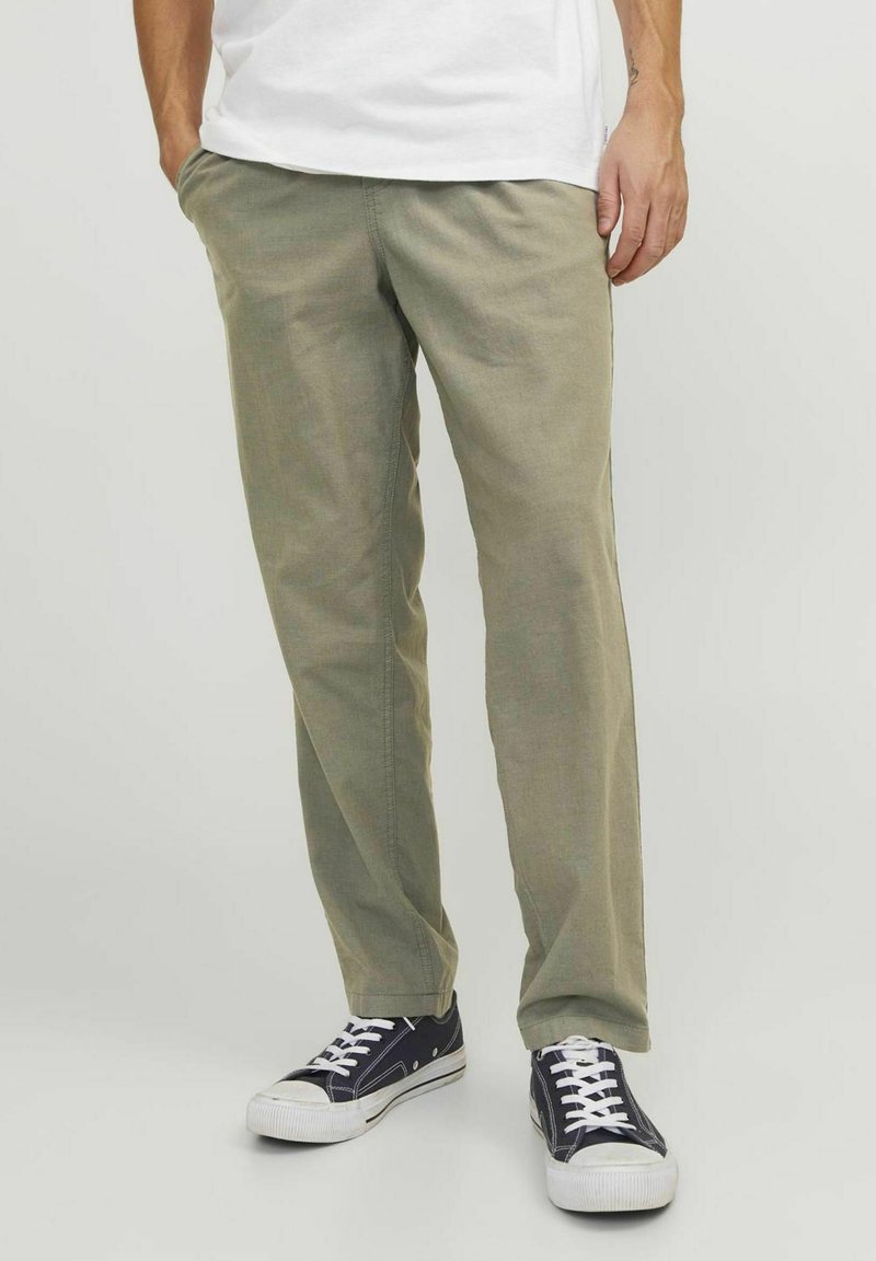Olivgrüne Chinos aus atmungsaktivem Stoff, mit einem lockeren Schnitt, seitlichen Taschen und kombiniert mit marineblauen Sneakers mit weißen Sohlen.