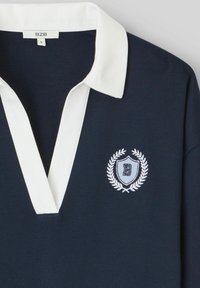 Polo shirt navy avec un col blanc et un logo de blason brodé arborant la lettre "B". Tissu doux avec un design classique.
