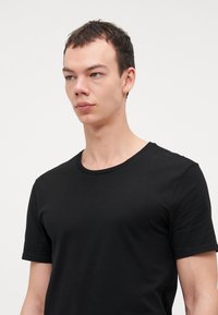 T-shirt nera a maniche corte con collo rotondo in tessuto morbido. Presenta un design semplice con taglio dritto.