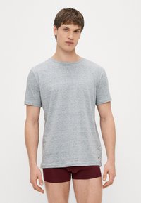 Γκρι κοντομάνικο μπλουζάκι από απαλό ύφασμα, με στρογγυλή λαιμόκοψη και ίσια γραμμή. Φορεμένο με μπορντό μπόξερ σορτς.