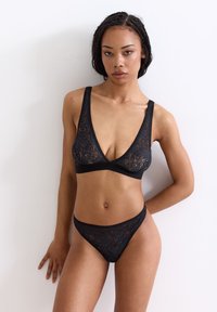 Black lace lingerie set featuring a deep V-neck bralette and matching thong. Floral pattern, adjustable straps, and soft texture.