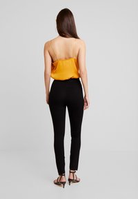 Černé legíny s vysokým pasem v kombinaci s hořčicovým saténovým topem na tenké ramínka a volnějším střihem. Přidány černé sandály na podpatku.