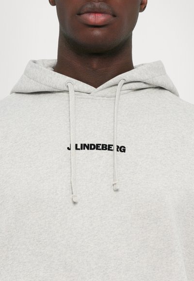 Hanorac gri dintr-un material moale, cu glugă ajustabilă și un logo negru "J Lindeberg" pe piept. Textură netedă, design casual.