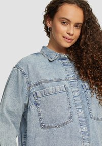Blauwe denim oversized overhemd met een spitse kraag, knopen aan de voorkant, twee borstzakken en een gestructureerde stof. Heeft opgerolde mouwen en gestikte details.