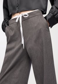 Szare szerokie spodnie wykonane z teksturowanej tkaniny z gładkim białym sznurkiem w talii. Koszula jest czarna, satynowa, z bufiastymi rękawami.