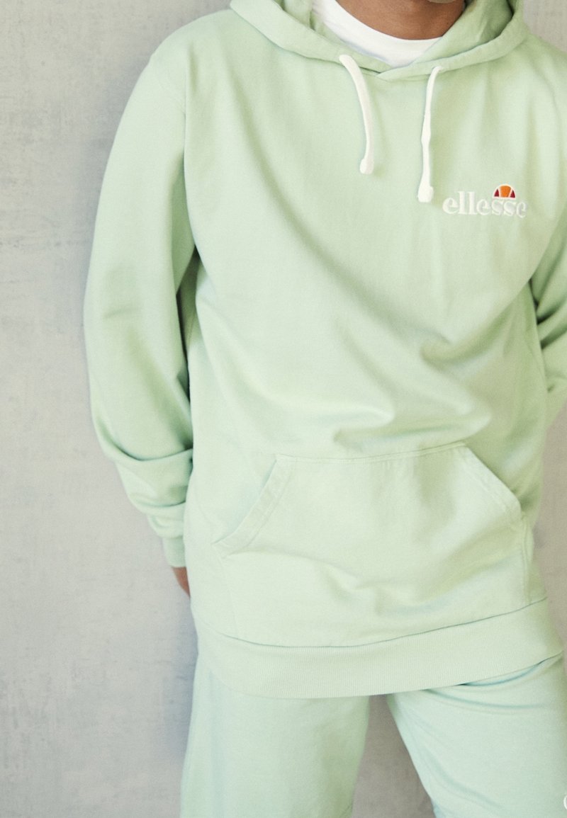 Felpa con cappuccio verde chiaro dotata di lacci, tasca a marsupio frontale e logo ricamato. Tessuto morbido con vestibilità comoda. Pantaloni coordinati.