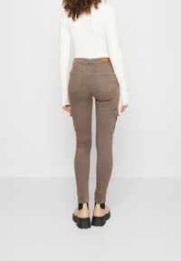 Brązowe spodnie cargo w slim fit, z tylnymi kieszeniami, bocznymi kieszeniami cargo i teksturowanym materiałem. Noszone z czarnymi i beżowymi butami.