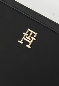 Superficie tessile nera con un prominente logo in metallo dorato caratterizzato da lettere interconnesse "H." Texture liscia, forma rettangolare, design minimalista.