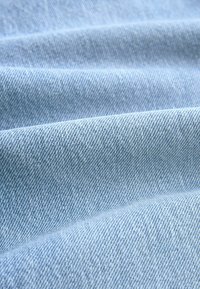 Heledsinine denimkangas, millel on herringbone muster, peene tekstuuriga ja pehme, sile pind. Lainejad lained loovad sügavuse.