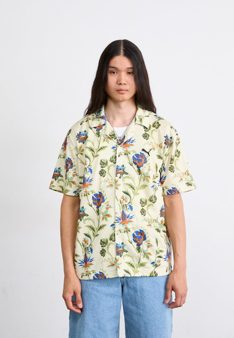 Korte mouwen, knoopshirt in lichtgeel met blauwe en oranje bloemenpatronen. Textuurstof met een relaxte pasvorm, gecombineerd met lichtblauwe jeans.